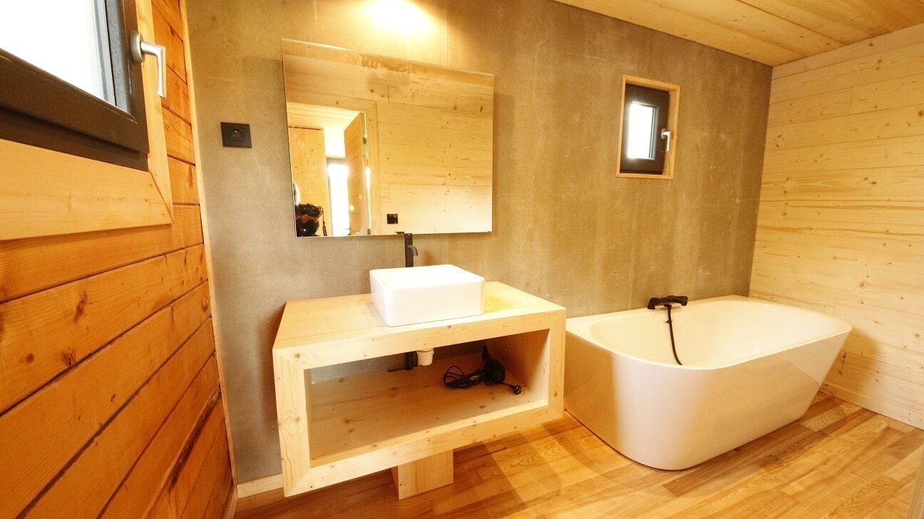 A wooden cabin bathroom with a sink, mirror, and bathtub.
