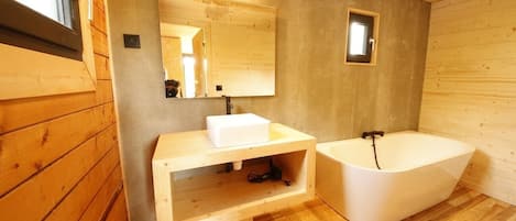 A wooden cabin bathroom with a sink, mirror, and bathtub.