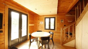 A wooden cabin interior with a dining table, chairs, a staircase, and large windows.