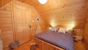 A wooden-paneled room with a bed, a door, a small picture, and a pair of boots.