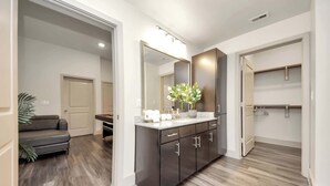 Un baño moderno con un mueble de tocador oscuro, un espejo grande y una zona de ducha.