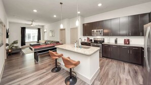 Una cocina moderna con armarios oscuros, una isla central con taburetes y una zona de comedor con mesa de billar.