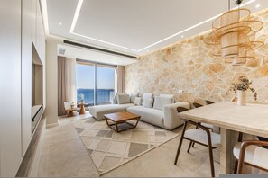 Ein modernes Wohnzimmer mit einer Steinwand, einem großen Fenster mit Blick, einem Sofa, einem Couchtisch und einem Essbereich.