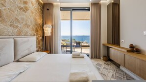 Een slaapkamer met een stenen muur, een bed, een badkamer met spiegel en uitzicht op zee.
