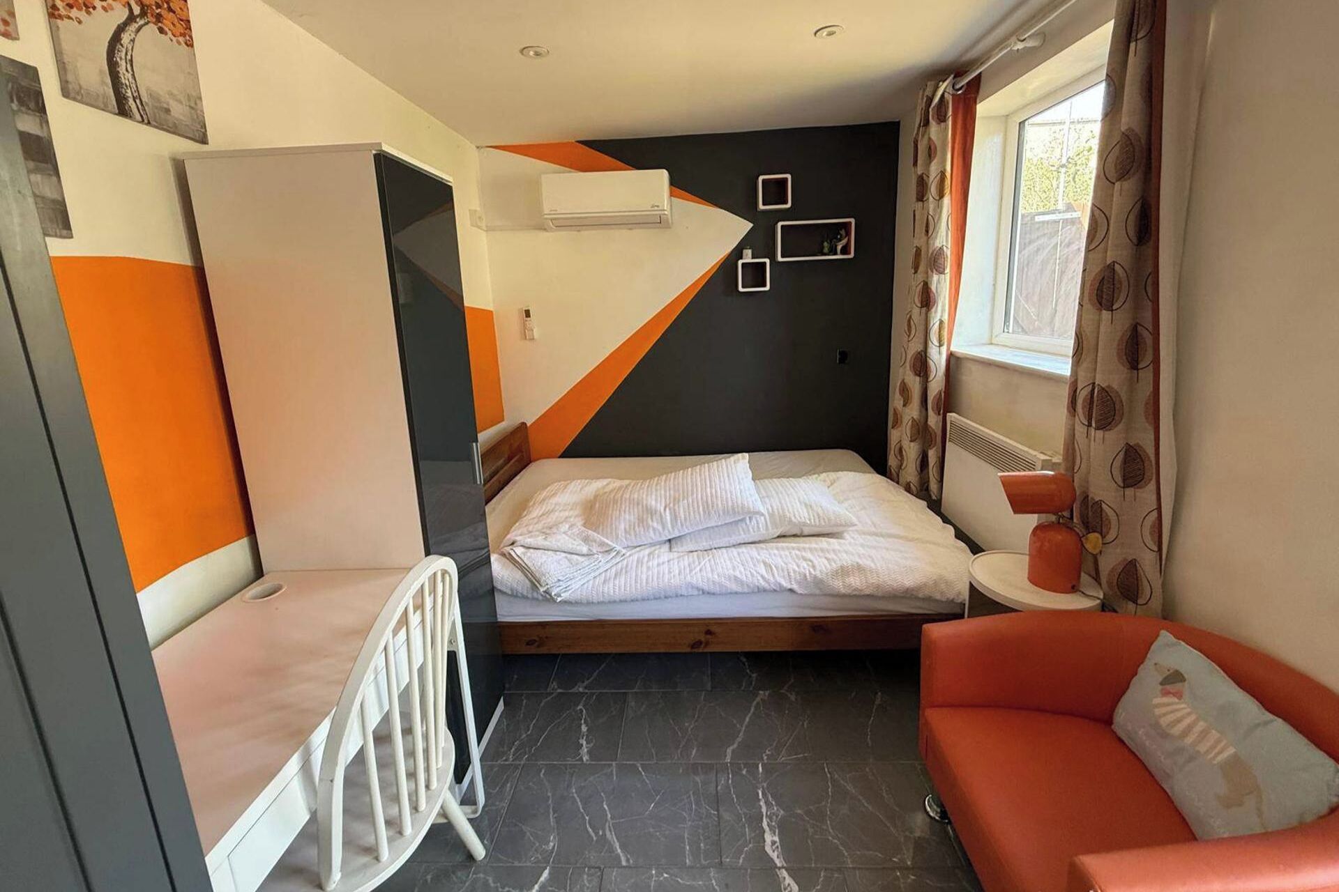 Une chambre d’hôtel de taille réduite, comprenant un lit, un petit coin salon, un radiateur et une fenêtre avec des rideaux.