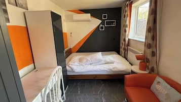 Une chambre d’hôtel de taille réduite, comprenant un lit, un petit coin salon, un radiateur et une fenêtre avec des rideaux.