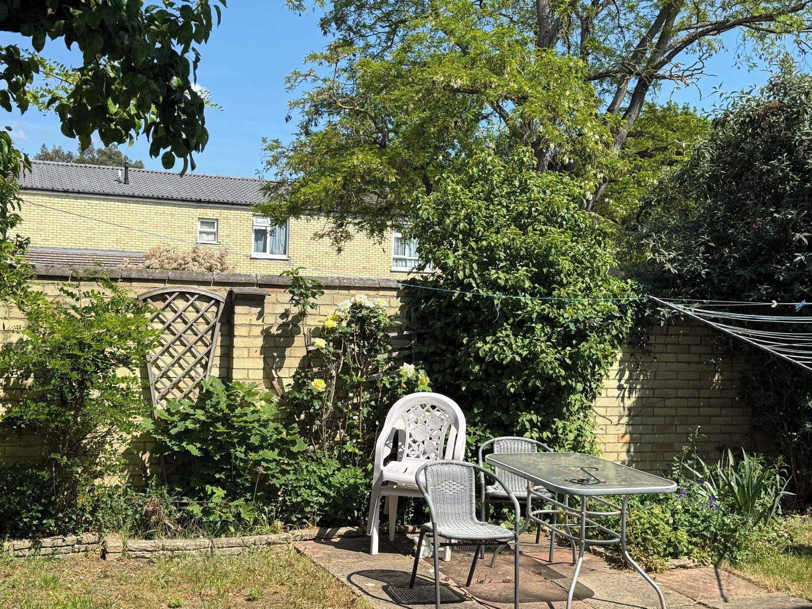 Une terrasse avec une table et des chaises, entourée de verdure et avec un bâtiment en arrière-plan.