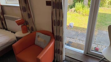 Une pièce avec un fauteuil rouge, une petite table ronde, un lit et une porte-fenêtre coulissante donnant sur un jardin.