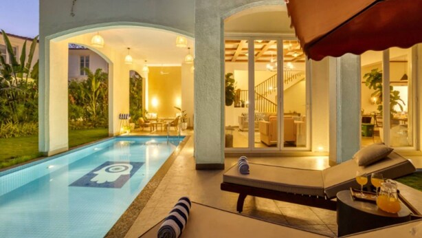 A swimming pool with a lifeguard symbol, lounge chairs, and a dining area with tables and chairs. - Villa Sai Shukhrana 3bhk w Private Pool in Moira (Moira)