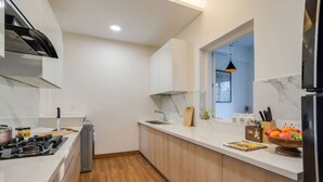 A modern kitchen with a gas stove, wooden cabinets, a window, and a fruit bowl. - Villa Sai Shukhrana 3bhk w Private Pool in Moira (Moira)