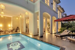 Ein Schwimmbecken mit dekorativem Fliesenmuster, Liegestühlen und einer überdachten Sitzgelegenheit mit rotem Sonnensegel.