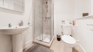 Ein Badezimmer mit einer Duschkabine, einem Waschbecken, einer Toilette und einem Spiegel.