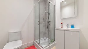 Een moderne badkamer met een glazen douchecabine, een wit toilet en een wastafel met toiletartikelen.