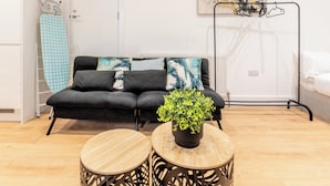 Een moderne woonkamer met een zwarte bank, twee ronde houten tafels, een potplant en een radiator.