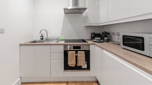 Een keuken met witte kastjes, een roestvrijstalen afzuigkap, een oven, een magnetron en een spoelbak.