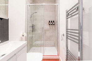A modern bathroom with a glass shower enclosure, a white sink, and a towel rack.