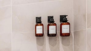 Trois bouteilles de gel douche sur un mur carrelé.
