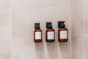 Three bottles of body wash on a tiled wall.