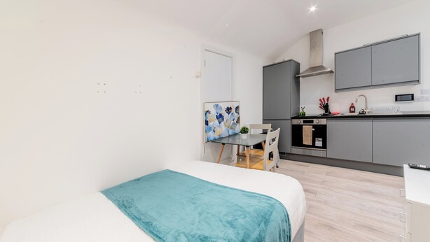 Une chambre à coucher comprenant un lit, un bureau, une chaise, un tableau et un coin cuisine.