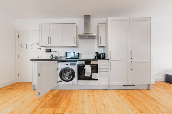 A compact kitchen with a washing machine, oven, microwave, and a coffee maker.