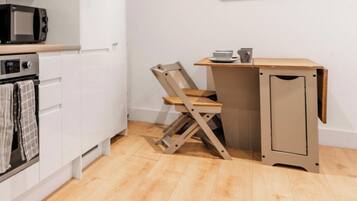 A compact kitchen with a microwave, oven, and a foldable chair.