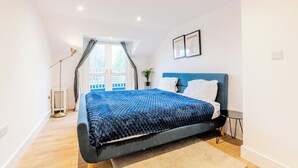 Une chambre à coucher avec un lit, une fenêtre avec des rideaux, une table de chevet et un luminaire fixé au mur.
