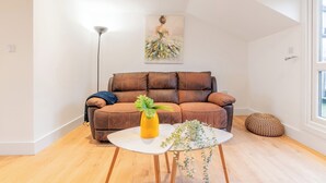 Un salon moderne avec un canapé en cuir marron, une table basse blanche ornée d’un vase jaune et un tableau accroché au-dessus du canapé.