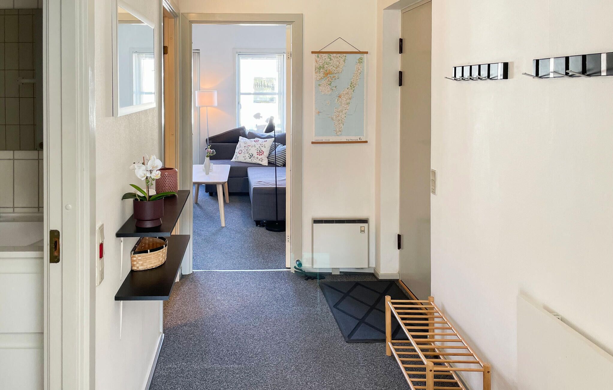 Un couloir avec un tapis noir, un porte-manteau en bois, une carte et un canapé au fond.