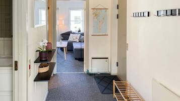 Un couloir avec un tapis noir, un porte-manteau en bois, une carte et un canapé au fond.