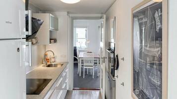 Un couloir étroit, avec une cuisine d’un côté, un coin repas avec une table et des chaises, et une grande image encadrée accrochée au mur.