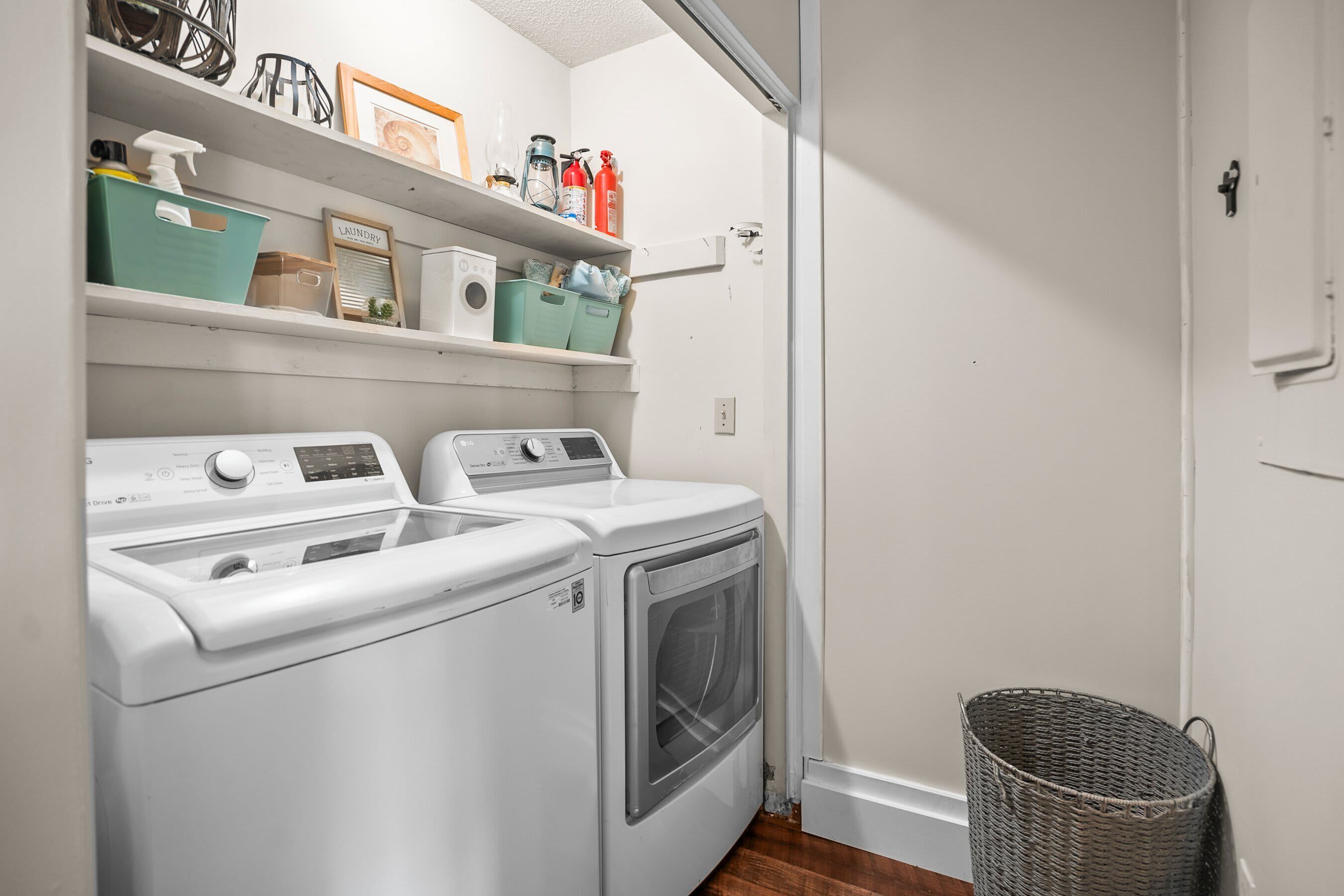 A laundry area with two front-loading washers, a dryer, shelves with cleaning supplies, and a wicker basket.