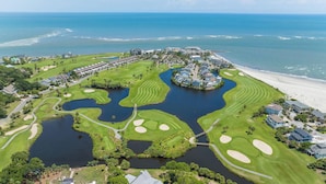Eine Vogelperspektive auf einen Golfplatz mit Wasserhindernissen, einem Strand und Wohnhäusern.