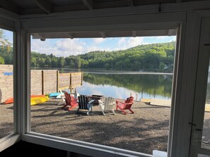 A view through a window of a lakeside deck with Adirondack chairs and a wooden dock. - Silver Lake Escape-Swim+Fish+Kayak+Relax in this lakefront Catskills Cottage! (Hancock)