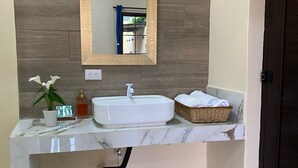 A bathroom with a white sink, a mirror, a potted plant, and a wicker basket.