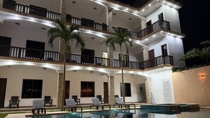 A multi-story building with a swimming pool, outdoor seating, and palm trees.
