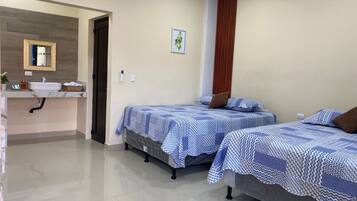 Habitación de hotel con dos camas, un baño con lavamanos y un espejo.