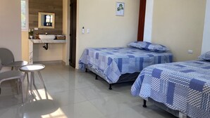 A hotel room with a bathroom, a bed with patterned bedding, a chair, and a small table.