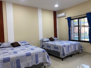 Habitación de hotel con dos camas, ventana con cortinas, unidad de aire acondicionado y vista al exterior.
