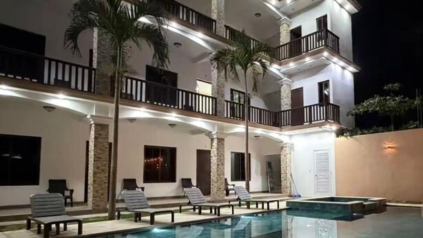 A multi-story building with a swimming pool, outdoor seating, and palm trees.
