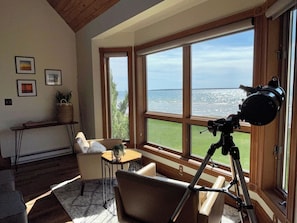 A room with a large window, a telescope, a sofa, a small table, and framed pictures on the wall.