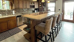 Una cocina amplia con armarios de madera, una isla grande con taburetes de bar, iluminación colgante y vistas al exterior.