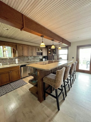 A spacious kitchen with wooden cabinets, a large island with bar stools, pendant lighting, and a view to the outside.