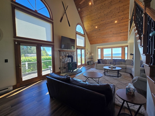 A spacious living room with a fireplace, large windows, a high ceiling, and a cozy seating area.