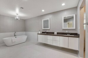 Un baño moderno con una bañera independiente, un tocador con espejo e iluminación empotrada en el techo.