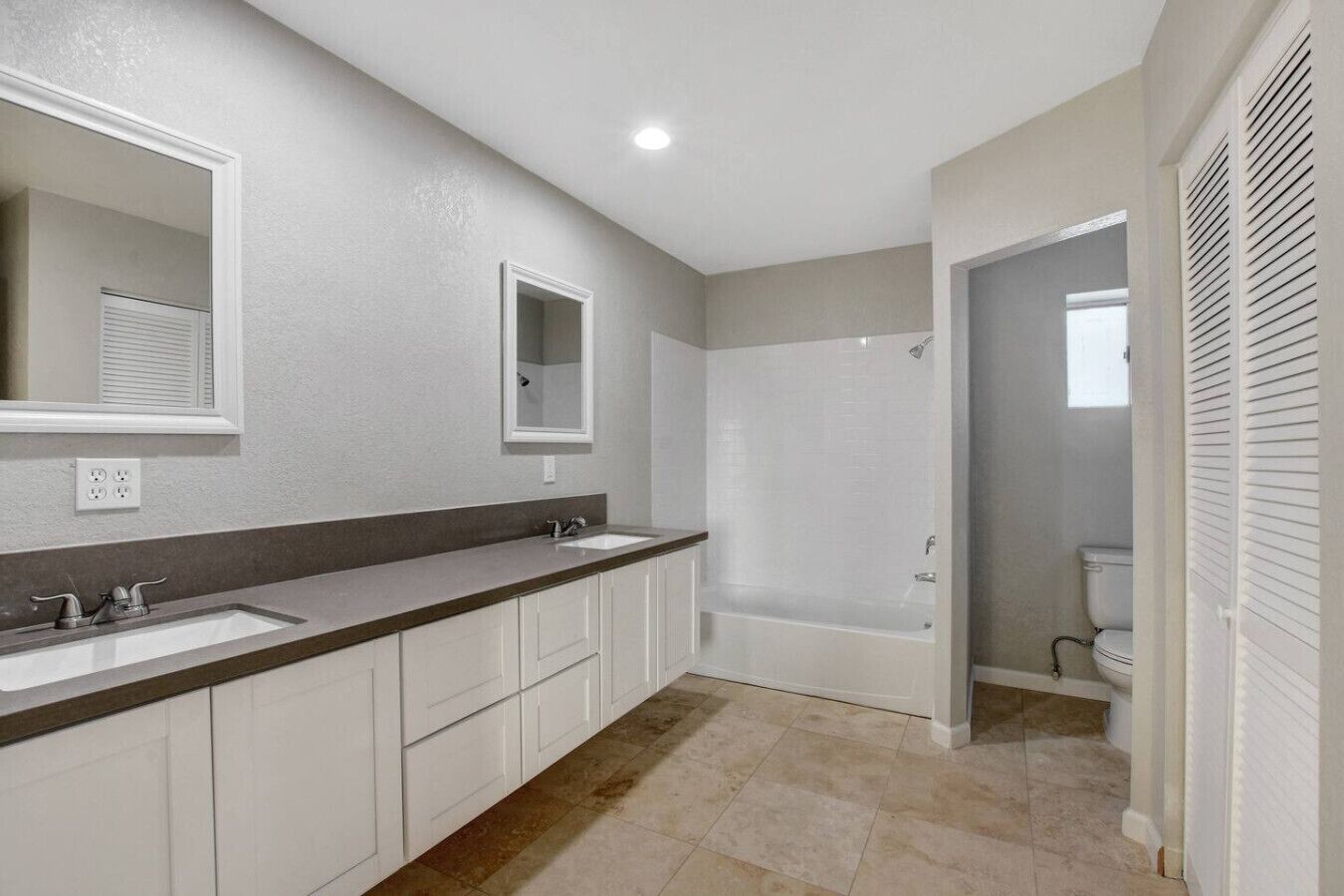 A bathroom with two sinks, a mirror, a shower, and a toilet.