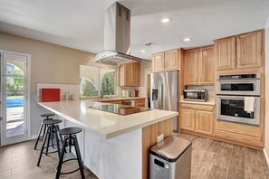 A modern kitchen with a central island, stainless steel appliances, wooden cabinets, and a view of the outdoors. - Las Vegas Quiet Compound (Las Vegas)