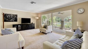 A living room with a flat-screen TV, a black entertainment unit, a white sofa, and a large window with a view of greenery. - Las Vegas Quiet Compound (Las Vegas)