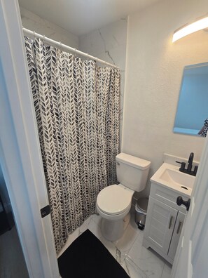 A bathroom with a shower curtain, toilet, sink, and cabinet. - Luxurious suits with independent entrance 15 mnts from the Strip (Las Vegas)