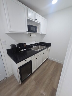 A compact kitchen with white cabinets, a black countertop, a built-in microwave, and a stainless steel sink. - Luxurious suits with independent entrance 15 mnts from the Strip (Las Vegas)