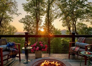 Eine Terrasse mit Feuerstelle, zwei Korbstühlen, einem Tisch mit Flasche und Glas sowie einem Blumentopf.